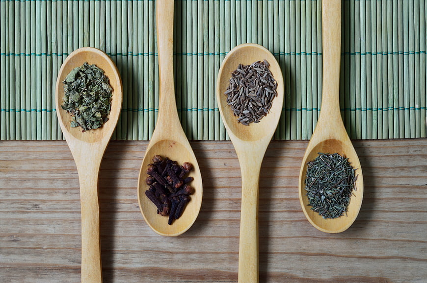 Wooden spoons with dried herbs and spices on bamboo mat