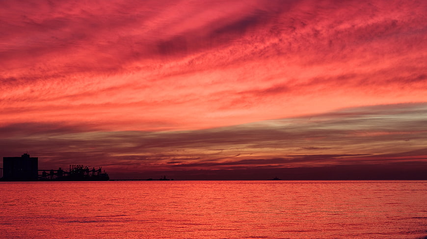 Vibrant Red Sunset Over Ocean with Silhouette of Port