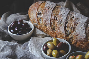 Rustic sourdough bread loaf with bowls of olives on linen