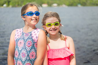 Two smiling girls in swimsuits and goggles by a lake