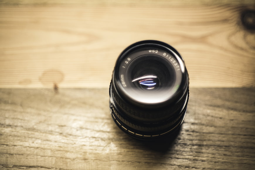 Black camera lens on wooden table with copyspace