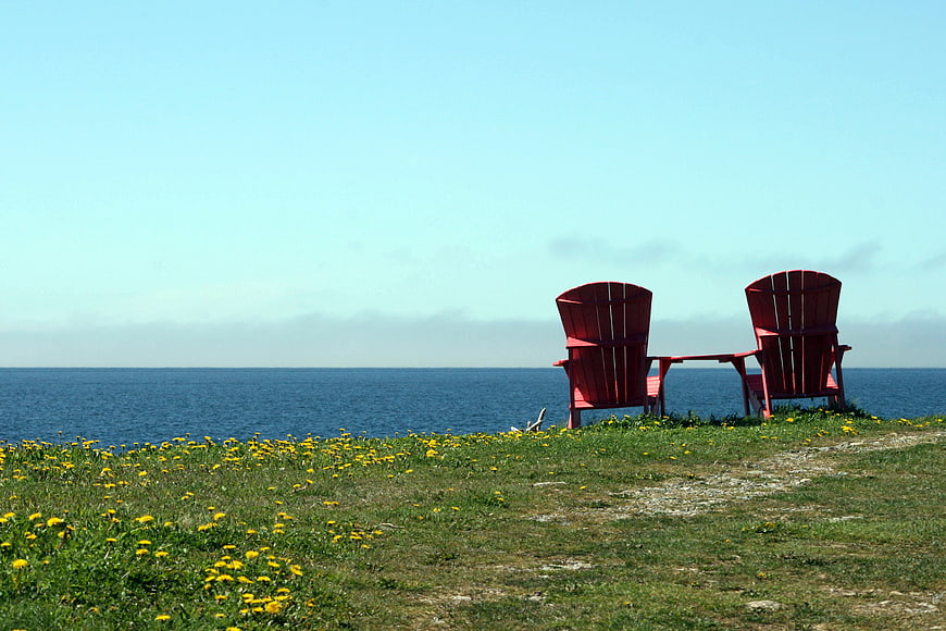 Red Adirondack Chairs Overlooking Ocean on Grassy Cliff