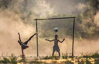 Children playing soccer in a misty river at golden hour
