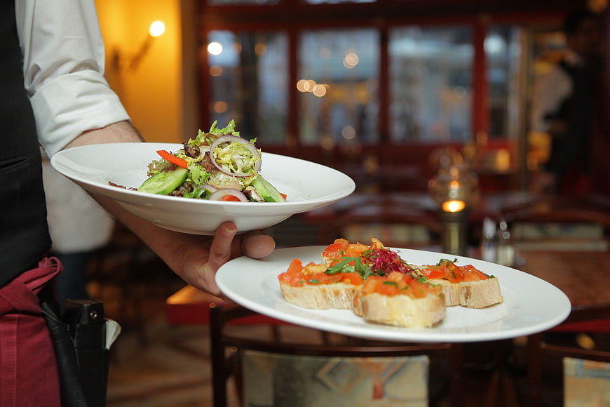 Waiter Holding Plates of Salad and Bruschetta in Restaurant