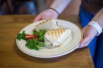 Waitress serving grilled wraps with strawberries on a wooden table