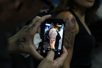 Tattoo artist photographing fresh sleeve tattoo on smartphone
