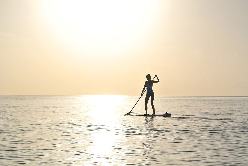 Woman Silhouette Paddleboarding on Calm Ocean at Sunset