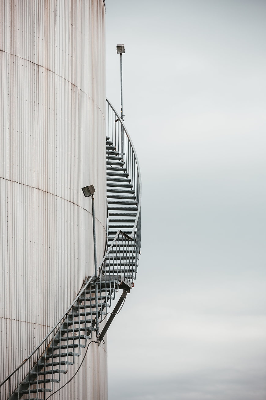 Curved metal staircase on industrial silo against gray sky