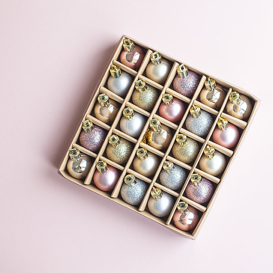 Box of pastel Christmas ornaments on pink background