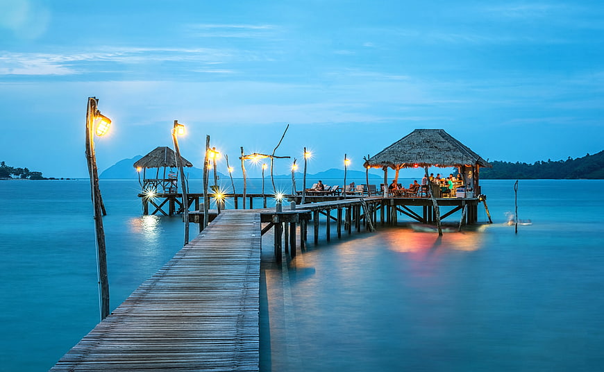 Illuminated wooden pier at twilight with thatched beach bar