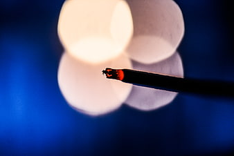 Close-up of burning incense stick with glowing ember against blue bokeh background