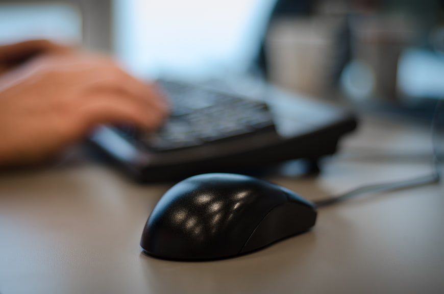 Close-up of black computer mouse on office desk with blurred typing hands