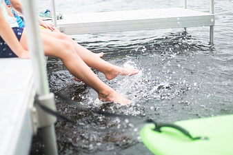 Children's legs splashing in lake water from dock