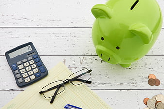 Green Piggy Bank, Calculator, and Glasses on White Wood