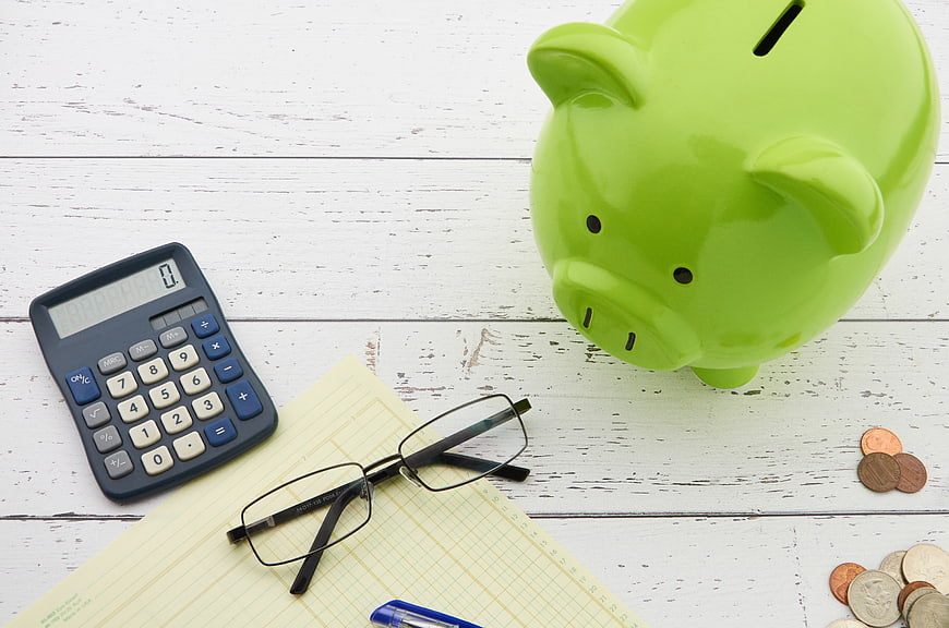 Green Piggy Bank, Calculator, and Glasses on White Wood