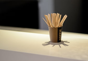 Cardboard cup with wooden coffee stirrers on white counter
