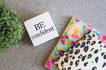 Flat lay of notebooks and 'Be confident' sign on gray background