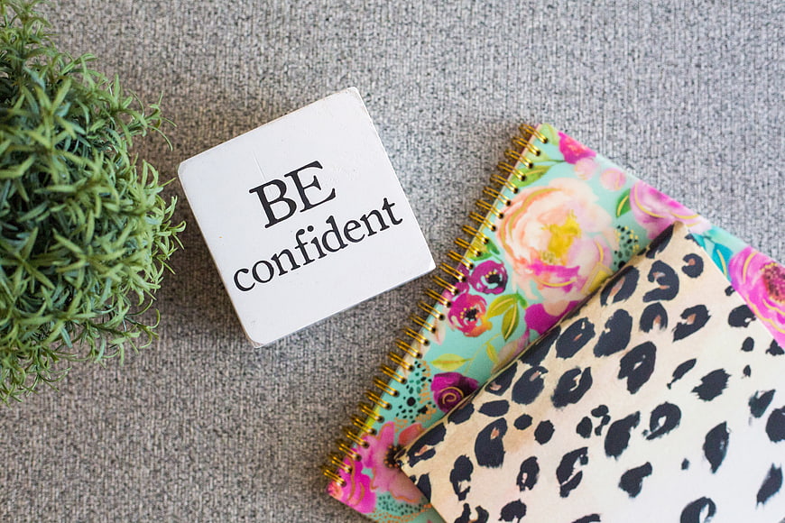 Flat lay of notebooks and 'Be confident' sign on gray background