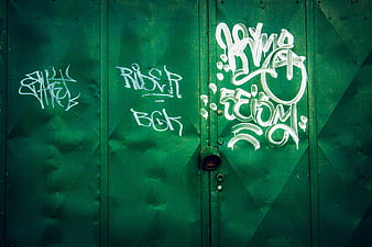White graffiti tags on a green corrugated metal wall