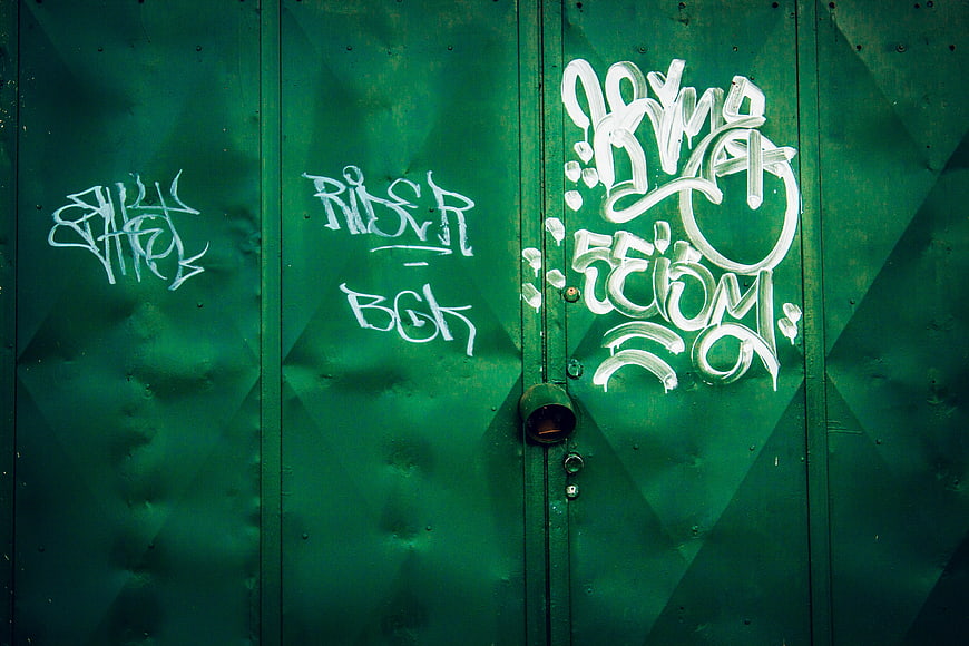White graffiti tags on a green corrugated metal wall