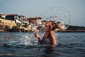 Woman Splashing Water in Sea with Coastal Town Background