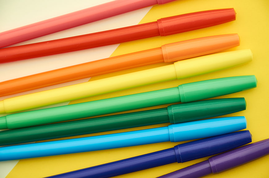Colorful markers arranged in rainbow order on yellow background