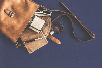 Flat lay of brown leather bag with accessories on blue background