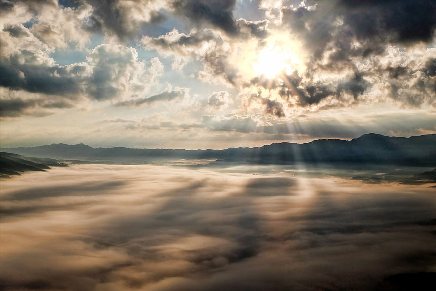 Sun rays piercing through clouds over a sea of fog