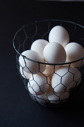 Fresh white eggs in a wire basket on dark background