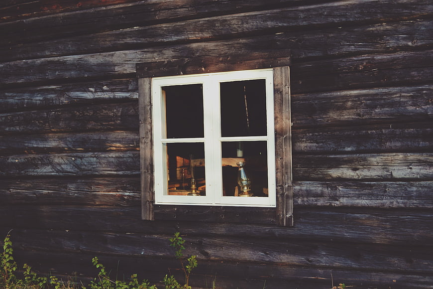 White window on weathered dark wooden cabin wall