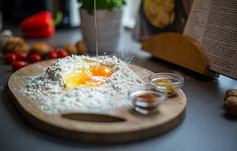 Cracking eggs into flour on wooden board with spices