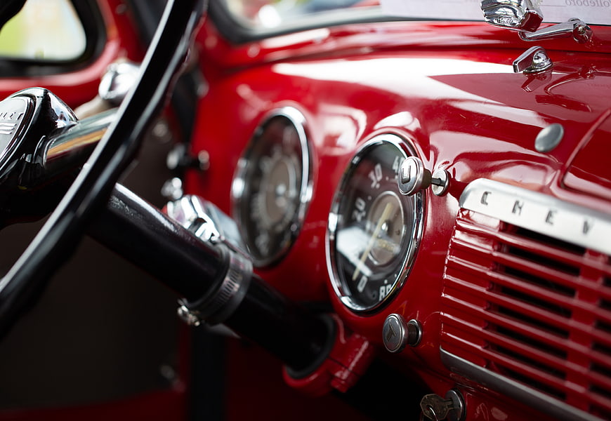 Close-up of vintage red Chevy dashboard with chrome gauges