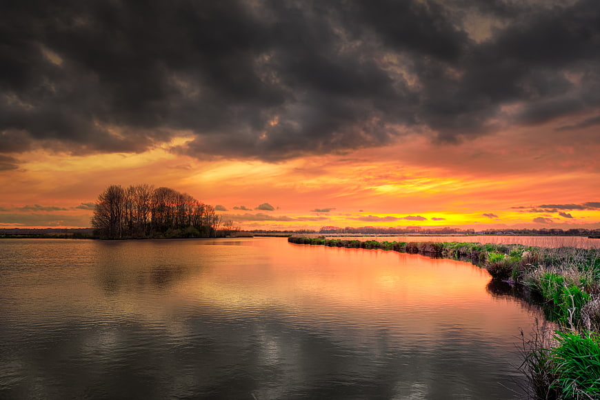 Dramatic sunset over river with dark clouds and vibrant orange sky
