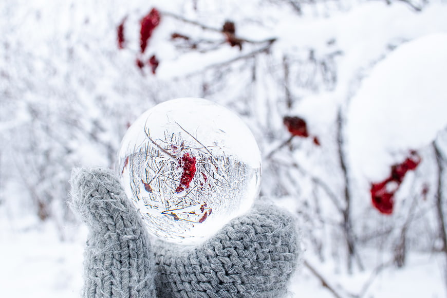 Hand in Grey Mitten Holding Ice Crystal Ball in Snowy Forest