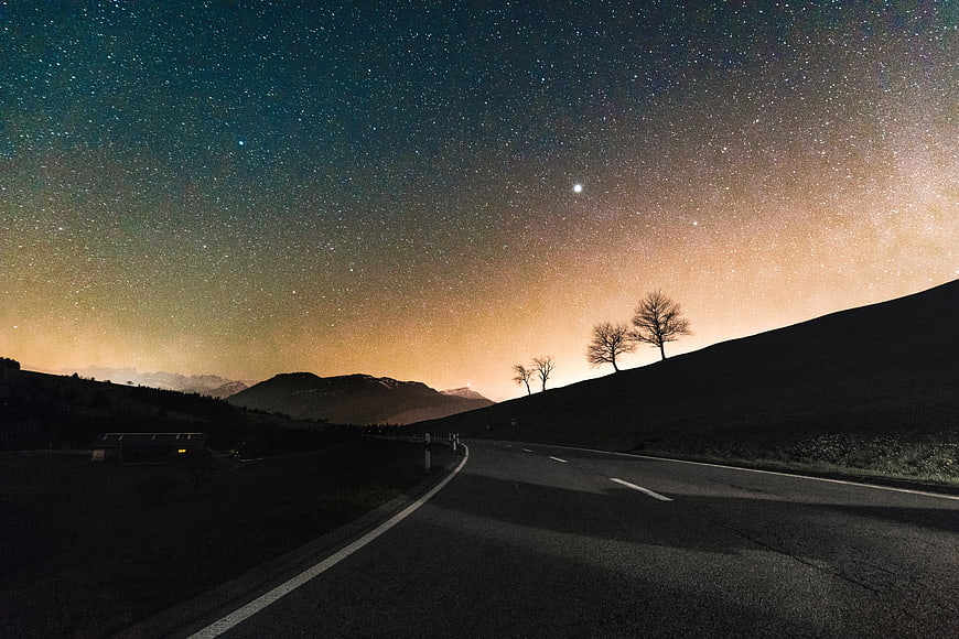 Starry Night Sky Over Winding Mountain Road with Silhouetted Trees