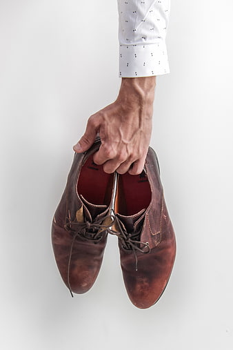 Hand holding brown leather dress shoes on white background