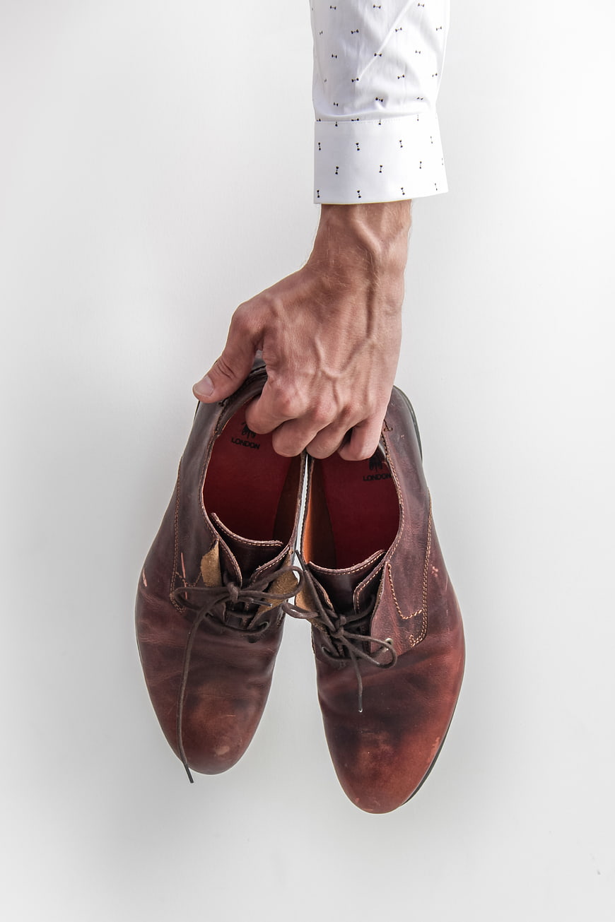 Hand holding brown leather dress shoes on white background