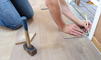 Carpenter measuring laminate flooring with pencil and hammer