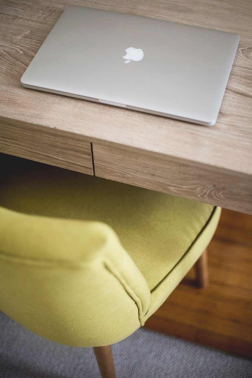Silver MacBook on wooden desk with yellow chair