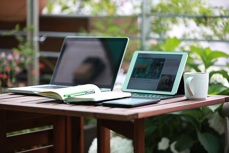 Outdoor workspace with laptop, tablet, and coffee on wooden table