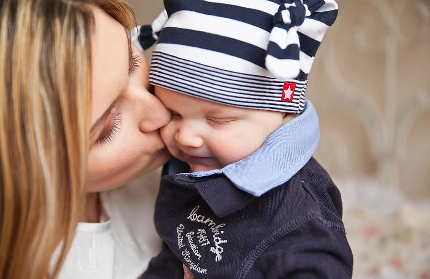 Mother Kissing Baby Wearing Striped Knit Cap