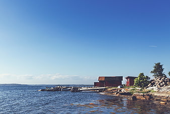 Red wooden boathouse on rocky island with blue sky