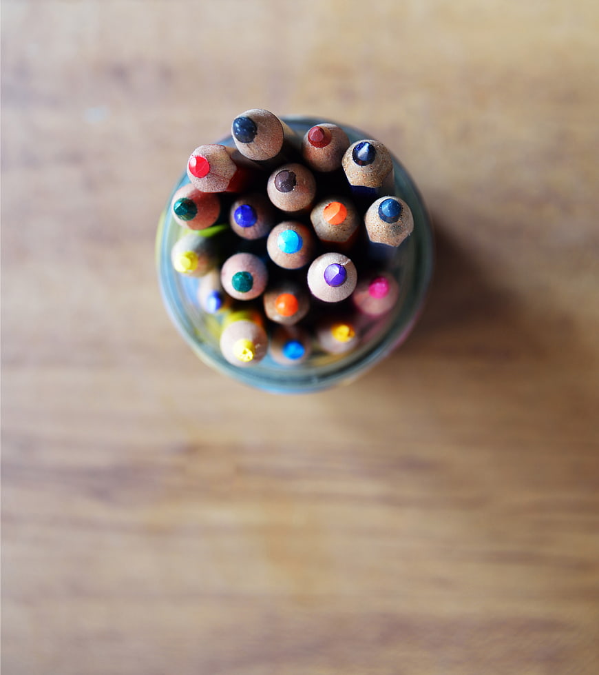 Top view of colorful pencils in a glass jar on wood