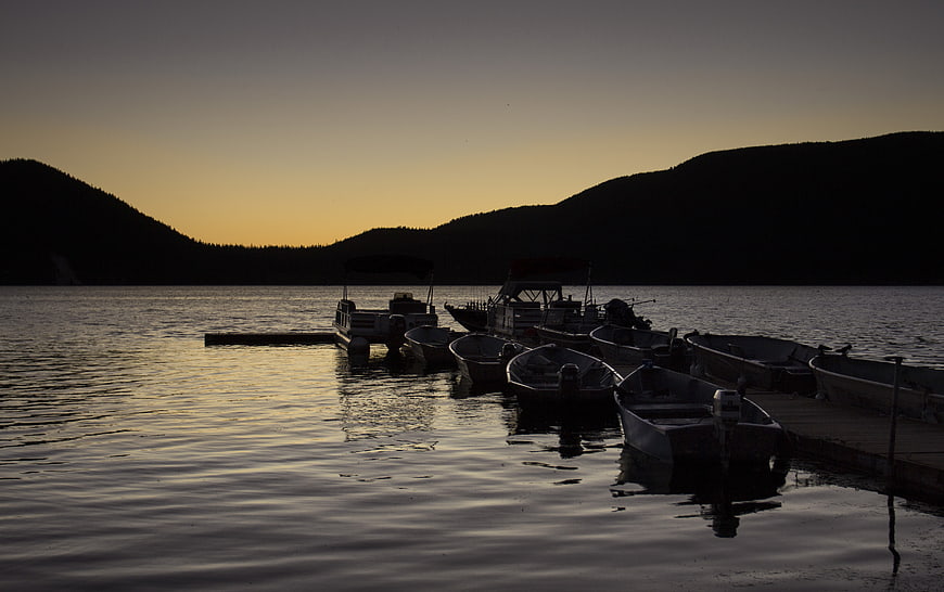 Silhouetted boats docked at sunset on a calm lake