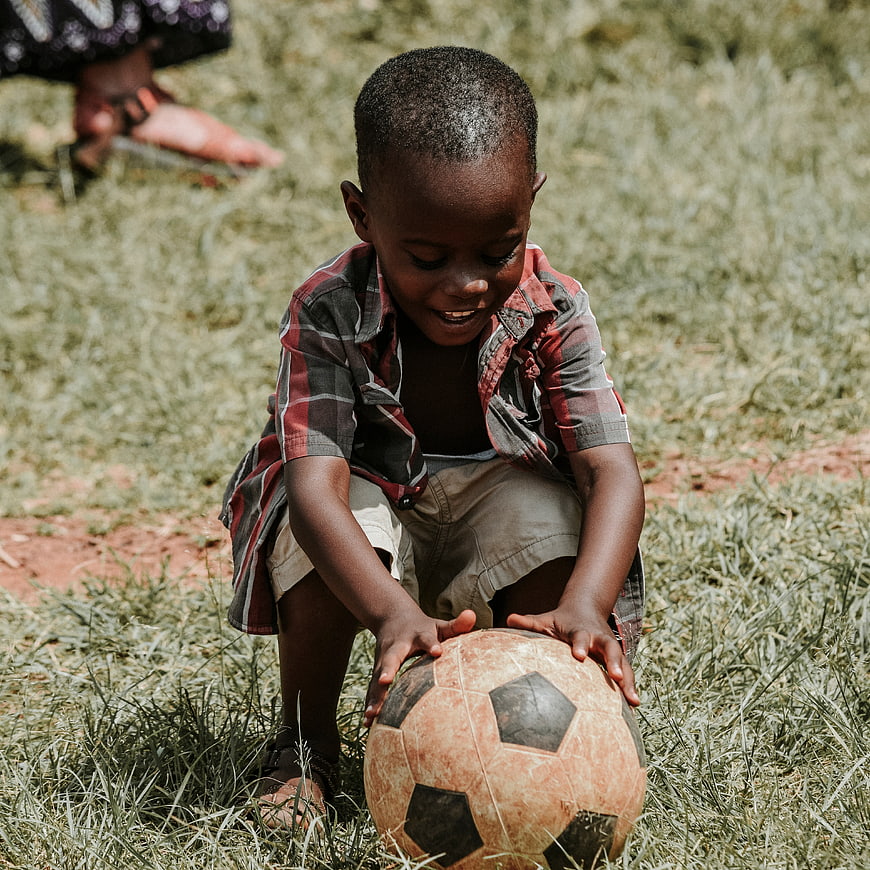Young African Boy Playing with Soccer Ball on Grass