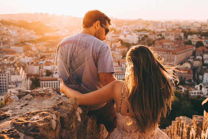 Couple embracing on rocky cliff overlooking city at sunset