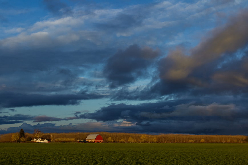 Red Barn in Green Field Under Dramatic Cloudy Sky