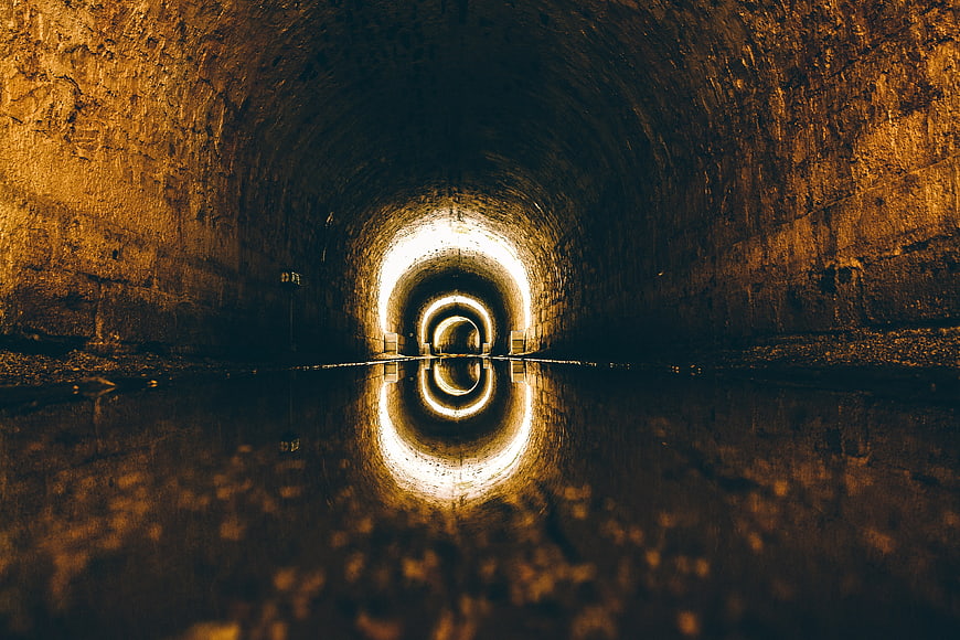 Dark tunnel with water reflection and light at the end