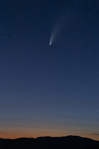 Comet streaking across twilight sky over mountain silhouette