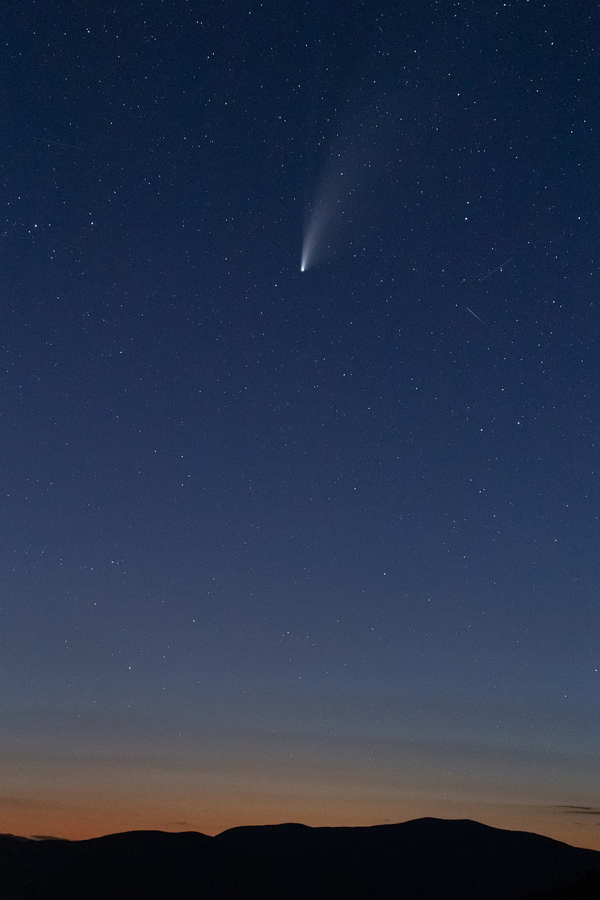 Comet streaking across twilight sky over mountain silhouette